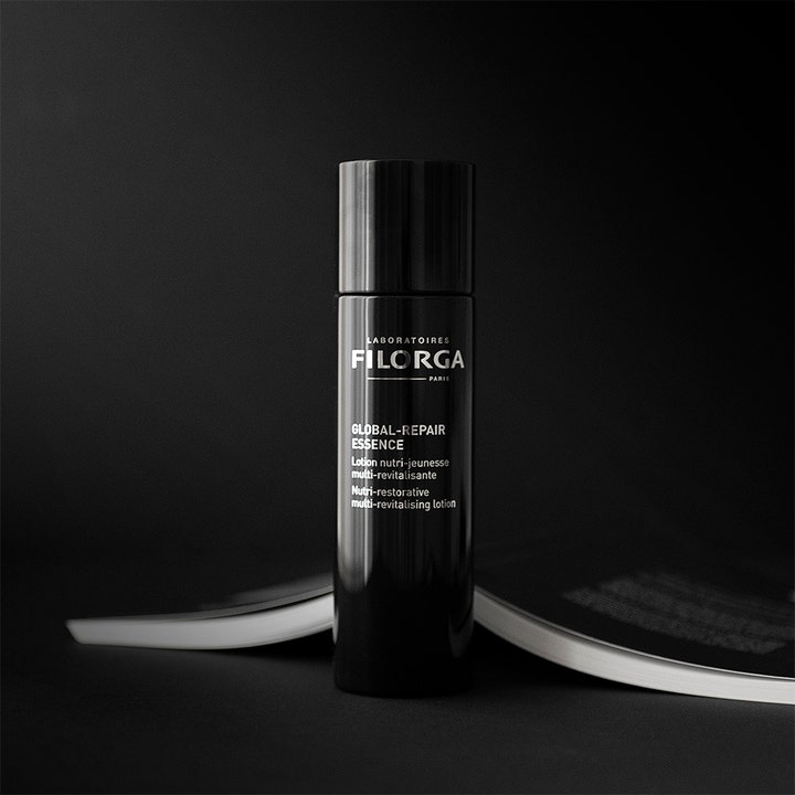 Filorga Global-Repair Essence 150 ml nærende ansigtspleje i elegant sort flaske foran en opslået bog