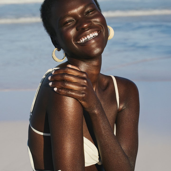 Sol de Janeiro Copacabana Bronze Glow Oil 75 ml glitrende kropsolie på en smilende kvinde ved stranden