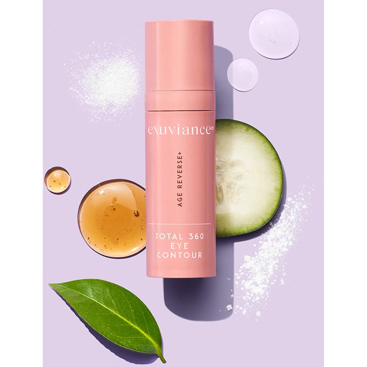 Exuviance Age Reverse Eye Contour 15 g øjencreme i lyserød tube vist med agurk og serum på lilla baggrund
