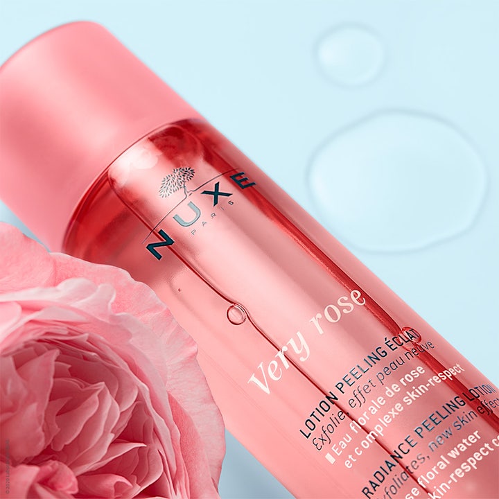 Nuxe Very Rose Peeling Lotion 150 ml eksfolierende peeling i lyserød flaske ved siden af en rose