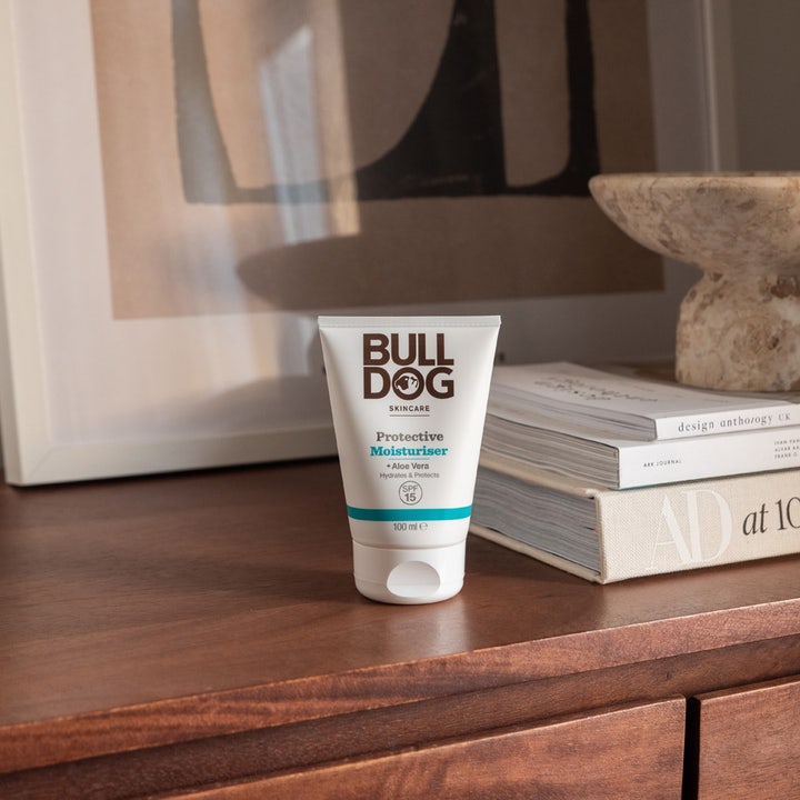 Bulldog Protective Moisturiser 100 ml fugtgivende dagcreme med SPF 15 i hvid tube på et træbord ved siden af bøger.