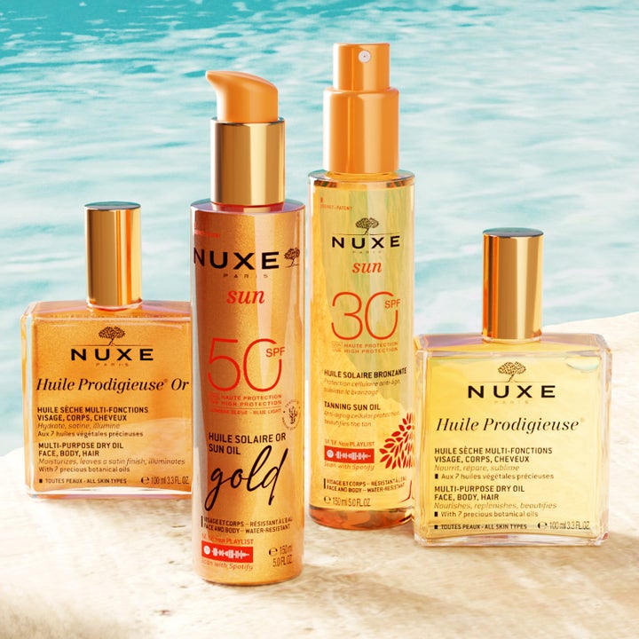 Nuxe Sun Tanning Oil Gold SPF50 150 ml i sprayflaske sammen med andre olier ved blåt vand
