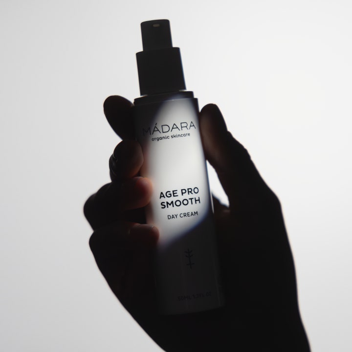 MÁDARA AGE PRO Smooth Day Cream 50 ml udglattende dagcreme i hvid pumpeflaske holdt af en hånd i silhuet.