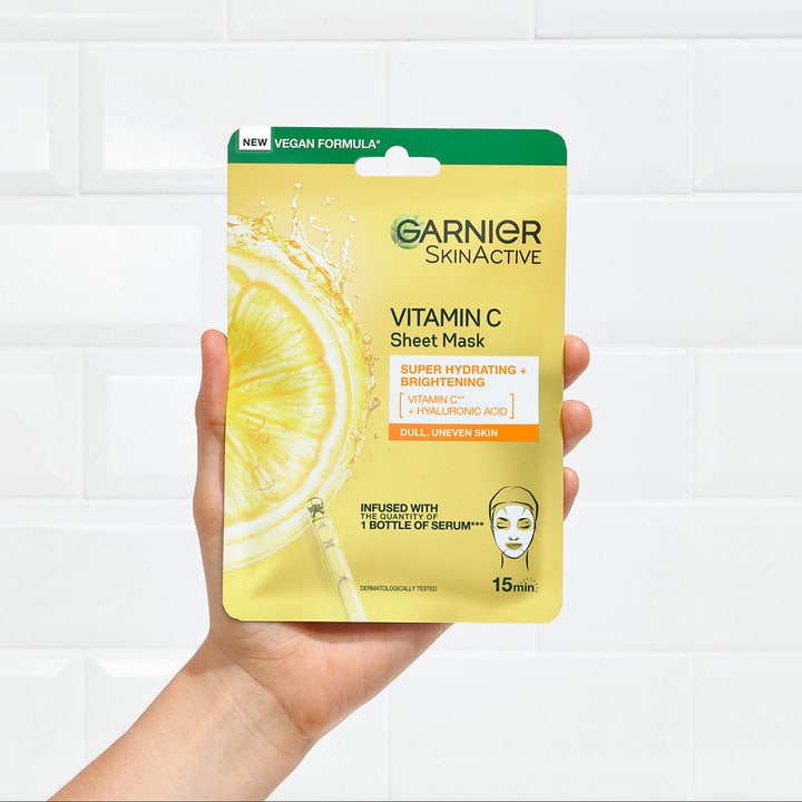 Garnier SkinActive Vitamin C Sheet Mask 28 g fugtgivende sheetmaske holdt i en hånd mod en hvid flisevæg