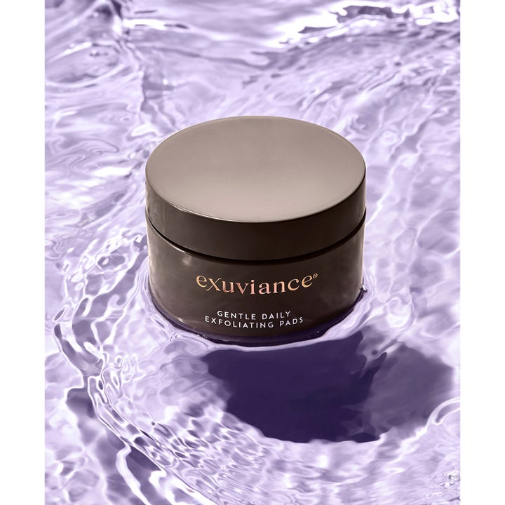 Exuviance Gentle Daily Exfoliating 60 Pads 55 ml eksfolierende pads i mørk krukke omgivet af lilla vand.