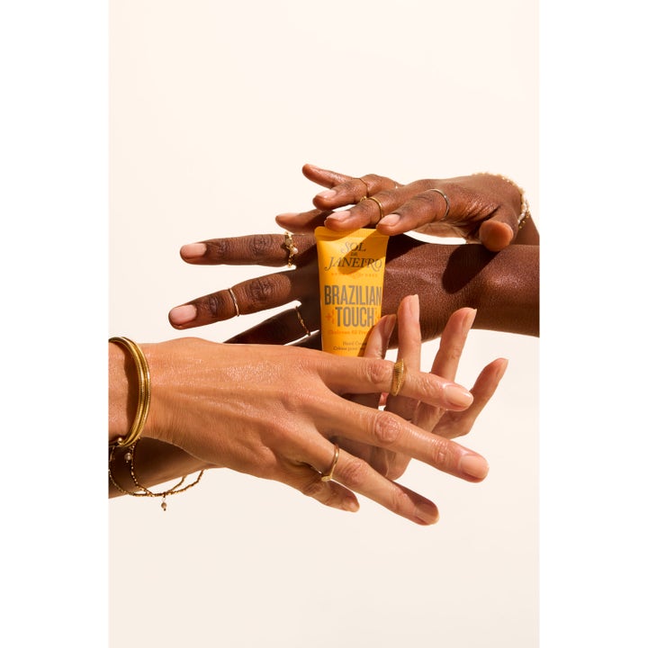 Sol de Janeiro Brazilian Touch Hand Cream 50 ml fugtgivende håndcreme i gul tube holdt af hænder med guldsmykker
