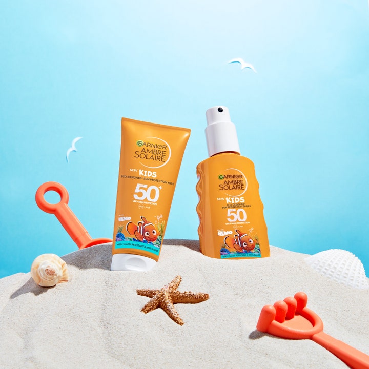 Garnier Ambre Solaire Kids 150 ml solbeskyttelse spray og tube med Nemo motiv i sandet med strandlegetøj