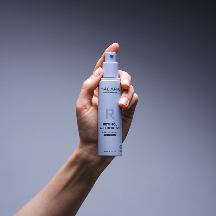 MÁDARA RETINOL ALTERNATIVE 50 ml natcreme i en lilla pumpeflaske holdt af en hånd mod en grå baggrund.