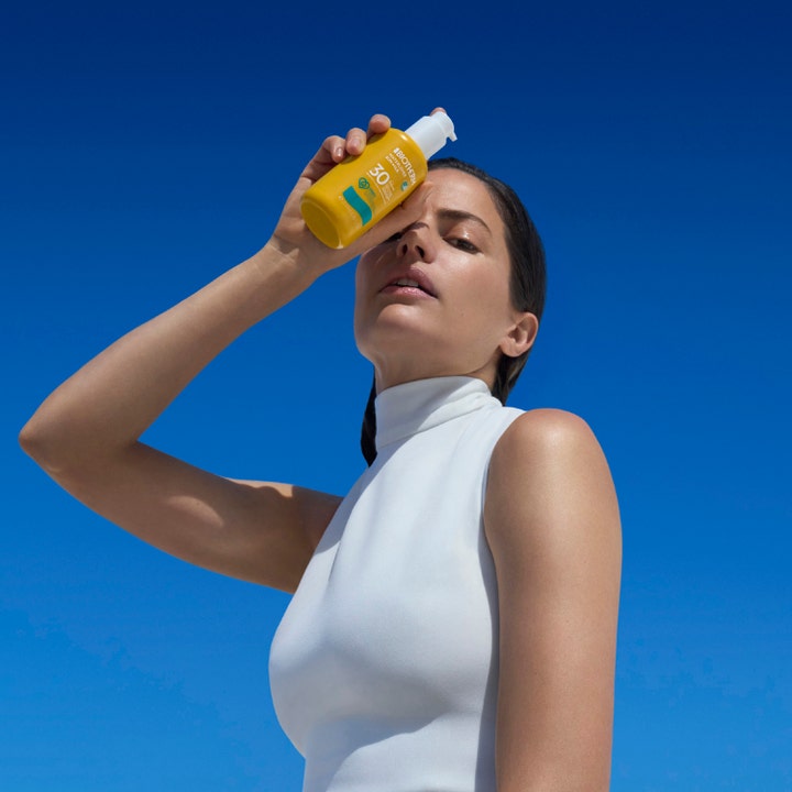 Biotherm Waterlover Sun Milk 200 ml fugtgivende solcreme i gul flaske holdt af en kvinde mod en blå himmel