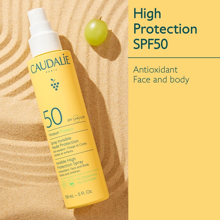 Caudalie Vinosun High Protection Spray SPF50 150 ml solcreme i gul sprayflaske på sand ved en vindrue.