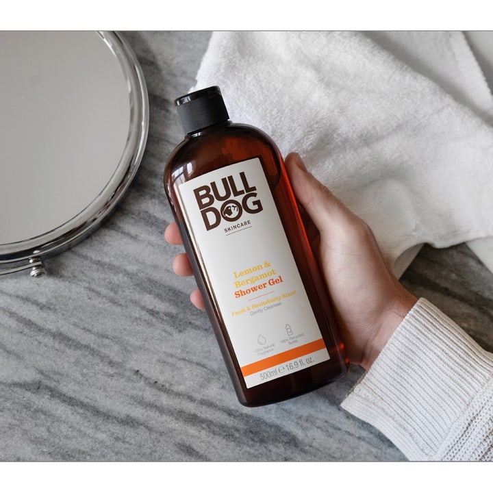 Bulldog Lemon & Bergamot Shower Gel 500 ml opfriskende brusegel i brun flaske holdt af en hånd ved et hvidt håndklæde.