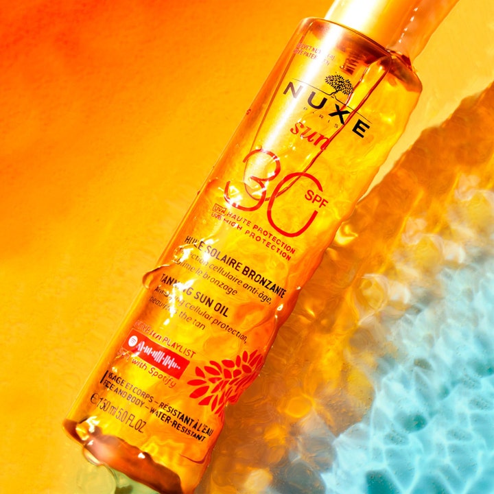 Nuxe Sun Tanning Oil 150 ml SPF 30 sololie til ansigt og krop i orange flaske i klart blåt vand med sollys