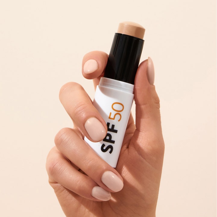 MÁDARA Pro-Active Mineral SPF50 Sunscreen Stick 12 g i hvid hylster holdes af en hånd med lys neglelak