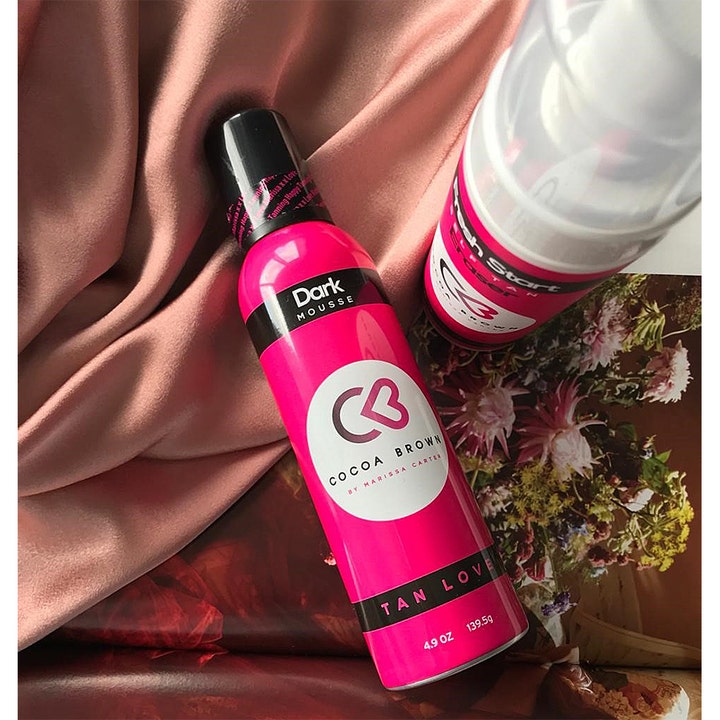 Cocoa Brown 1 Hour Tan Dark 150 ml selvbruner mousse i pink sprayflaske på silkestof og blomsterbaggrund