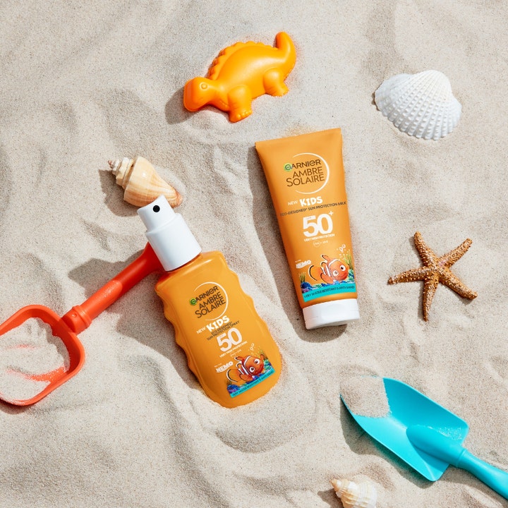 Garnier Ambre Solaire Kids Sun Protection Spray 150 ml solcreme til børn SPF 50 orange flaske i sandet med legetøj