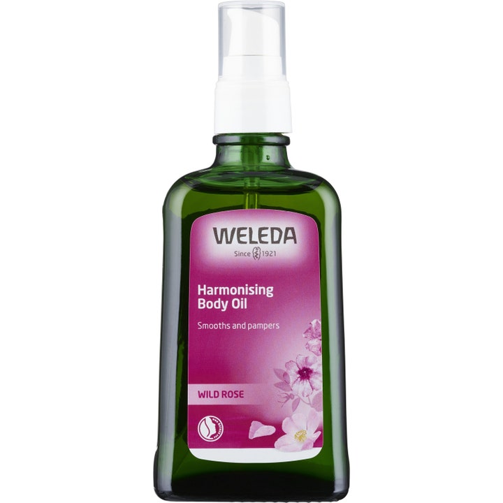 Weleda Wild Rose Harmonising Body Oil 100 ml harmoniserende kropsolie i grøn glasflaske med hvid pumpe og lilla roser