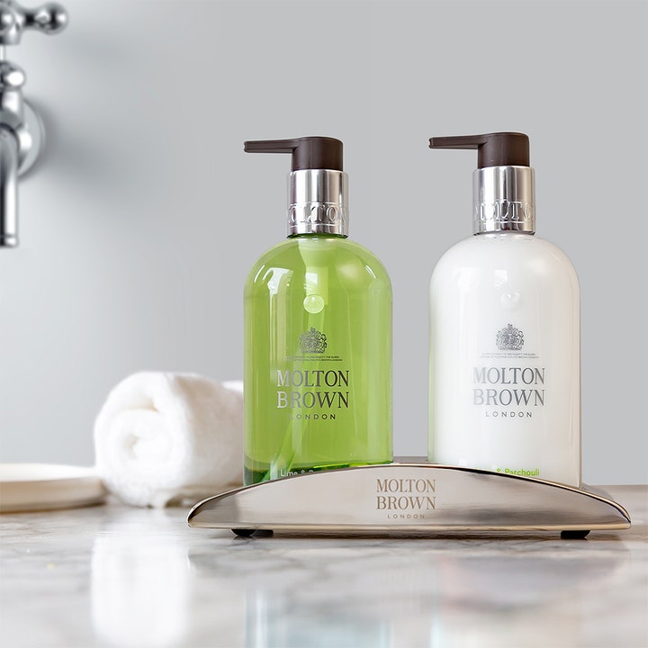 Molton Brown Lime & Patchouli Hand Lotion 300 ml fugtgivende håndpleje i hvid flaske i en elegant sølvholder