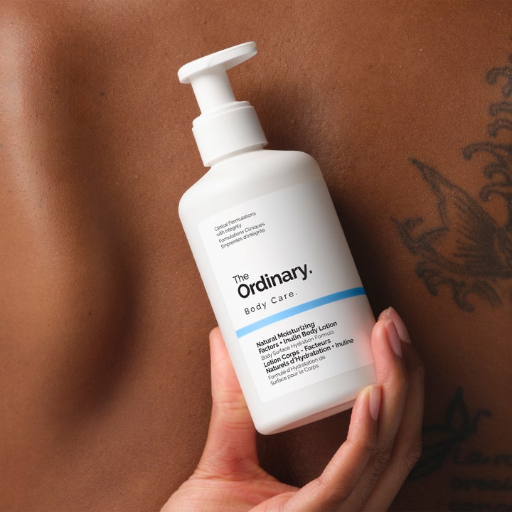 The Ordinary NMF + Inulin Body Lotion 240 ml fugtgivende bodylotion i hvid pumpeflaske holdt mod bar hud