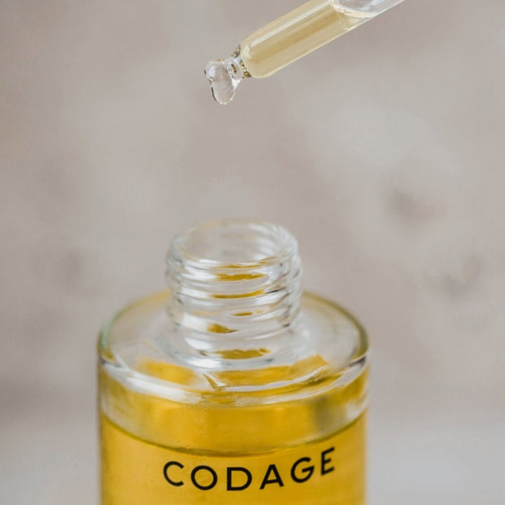 Codage Paris The Oil 100 ml nærende kropsolie i glasflaske med pipette der drypper en gylden dråbe