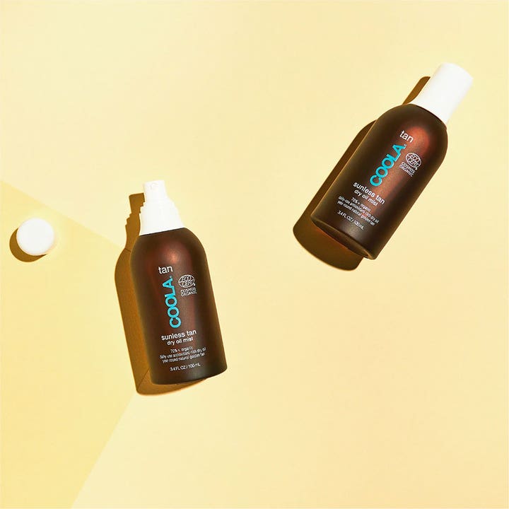 COOLA Sunless Tan Dry Oil Mist 100 ml økologisk selvbruner i brune sprayflasker vist på en gul baggrund.