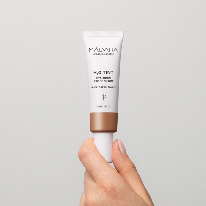 MÁDARA H2O Tint 30 ml farvet serum giver fugt i en hvid tube holdt af en hånd mod grå baggrund