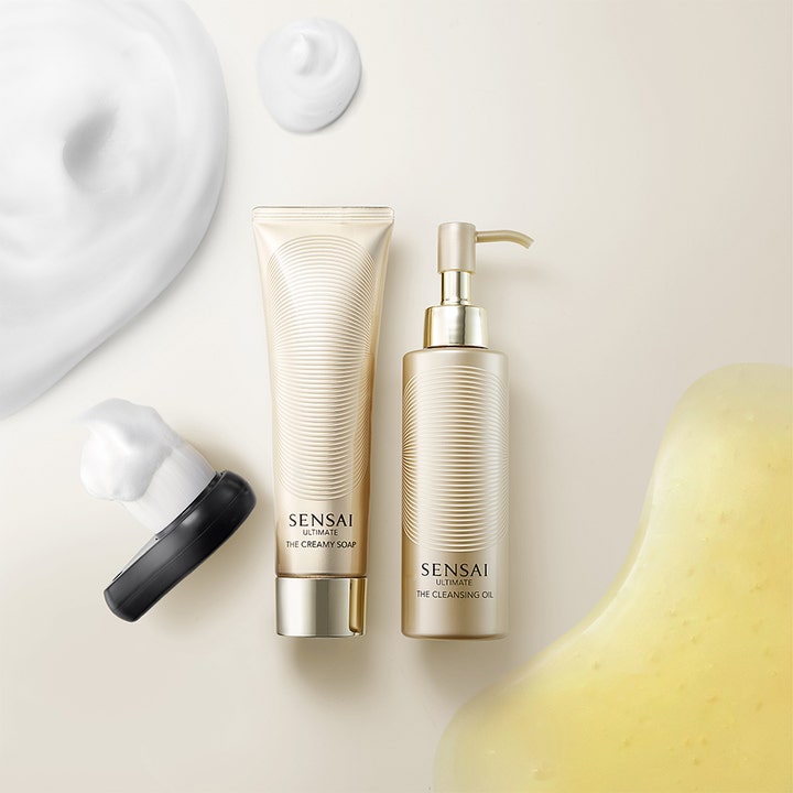 Sensai Ultimate The Cleansing Oil 150 ml ansigtsrens i guldflaske vist med gylden olietekstur og hvidt renseskum