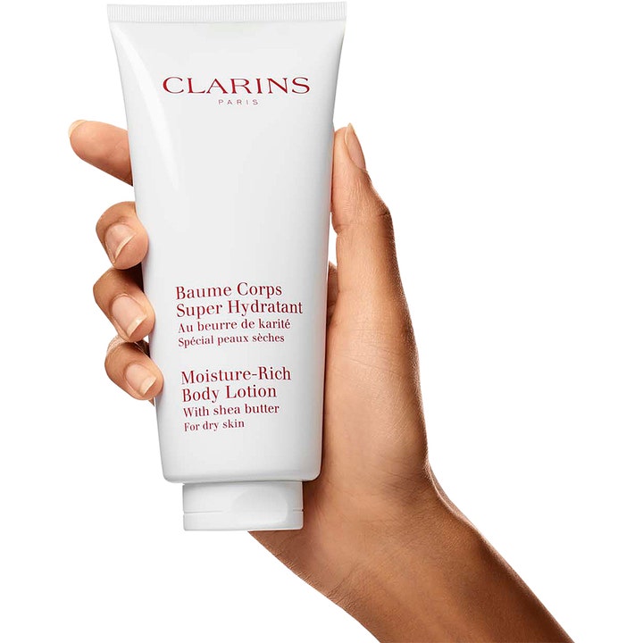 Clarins Moisture-Rich Body Lotion 200 ml fugtgivende bodylotion med sheasmør til tør hud i hvid tube holdt af en hånd