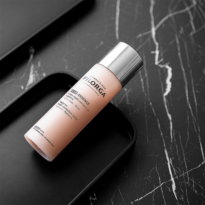 Filorga NCEF-Essence 150 ml fugtgivende ansigtslotion i rosa flaske med sølvlåg på sort marmor.