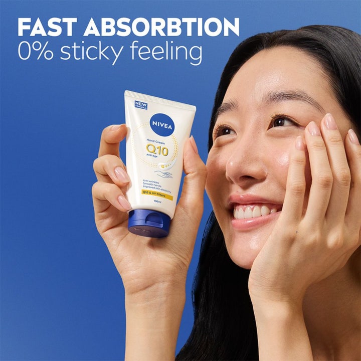 Smilende kvinde holder NIVEA Q10 Hand Cream 100 ml anti-age håndcreme i tube med hurtig absorbering