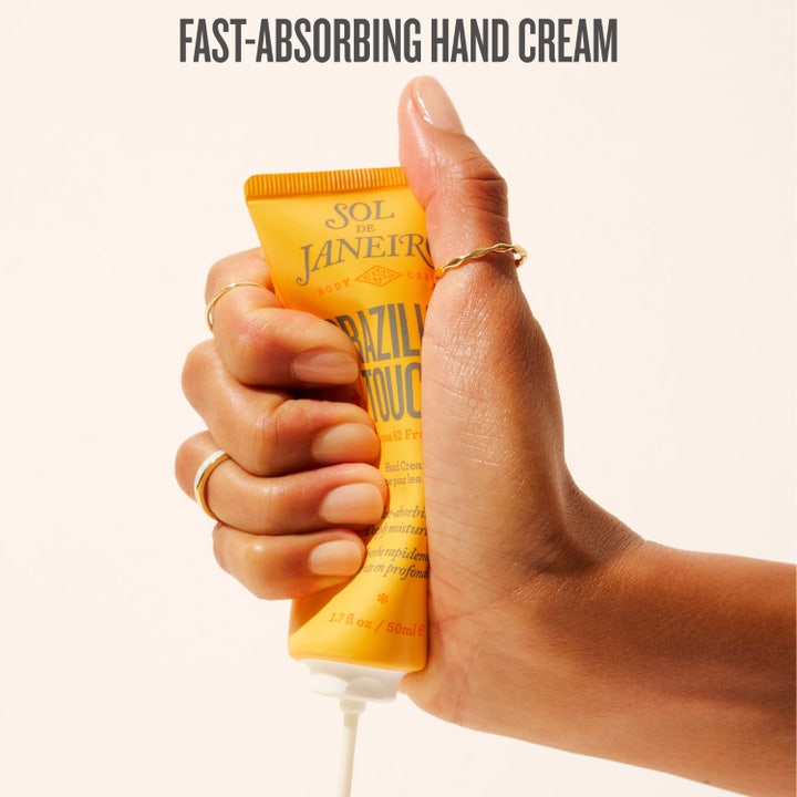 Sol de Janeiro Brazilian Touch Hand Cream 50 ml fugtgivende håndcreme i gul tube holdt af hænder med forskellige hudtoner