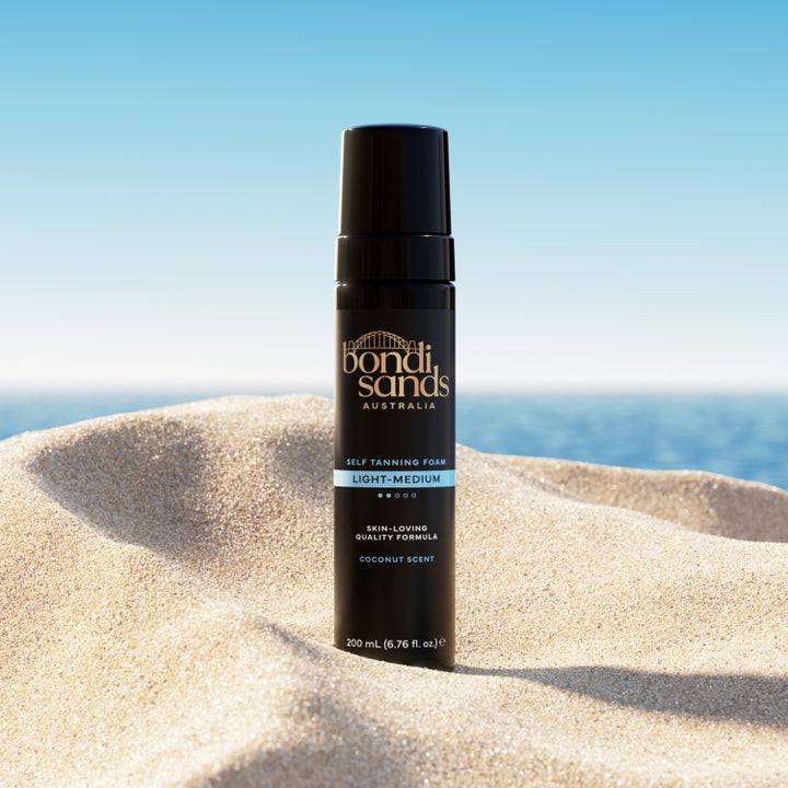 Bondi Sands Self Tanning Foam Light Medium 200 ml i sort flaske på en solskinsstrand der giver glød
